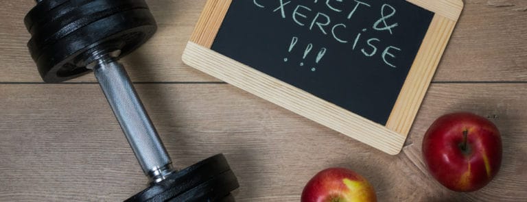 A weight, some apples, and a chalkboard with diet & exercise written on it