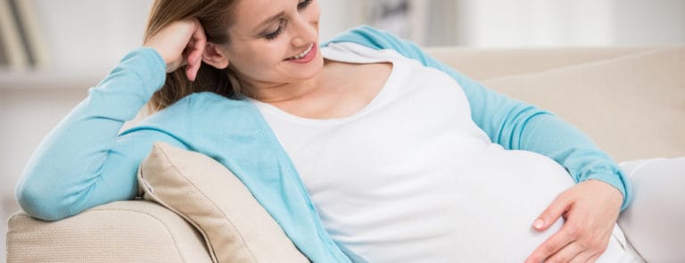 Pregnant woman sitting at sofa and keeping hand on belly