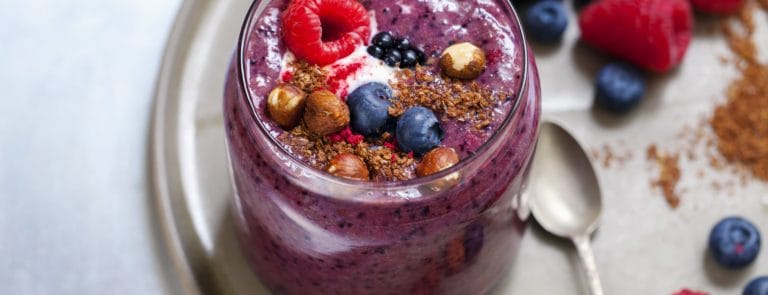 Jar of purple flaxseed smoothie topped with berries and nuts