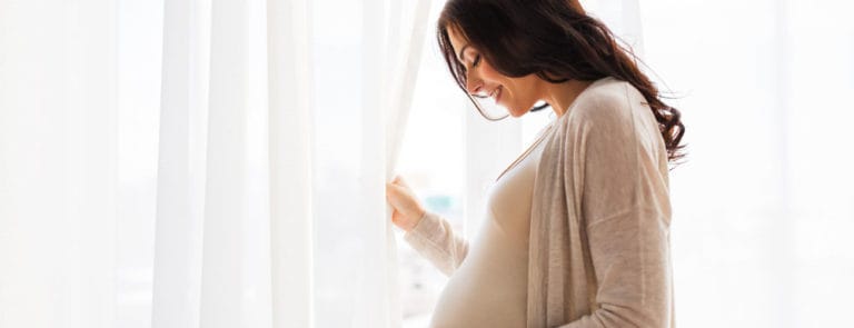 Pregnant woman smiling with hand on bump