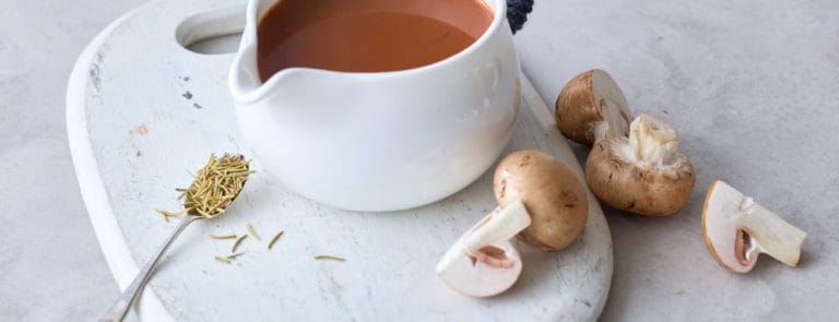 A pouring bowl containing vegan gravy with mushrooms on the side