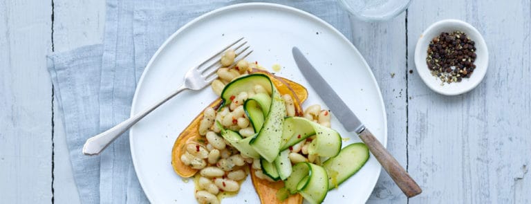 Sweet potato with white beans and courgette on a plate with a knife and fork