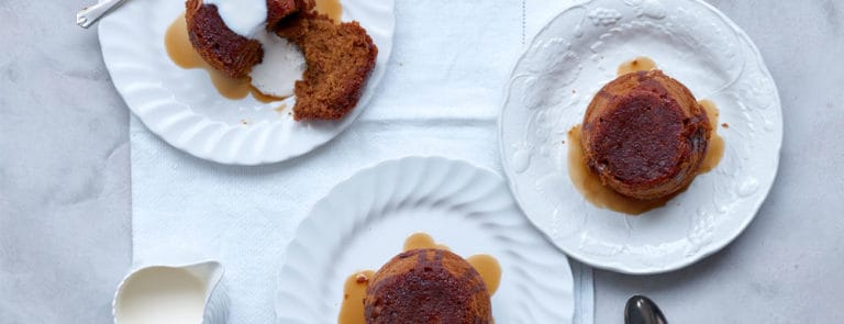 Three sticky toffee puddings made with dates, served with toffee sauce and pouring cream