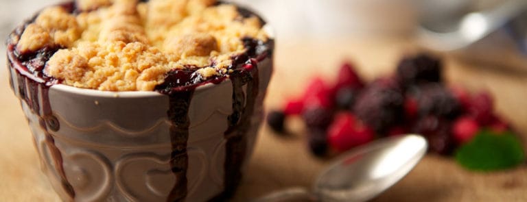 Crumble in a ceramic pot next to a handful of berries on a wooden board