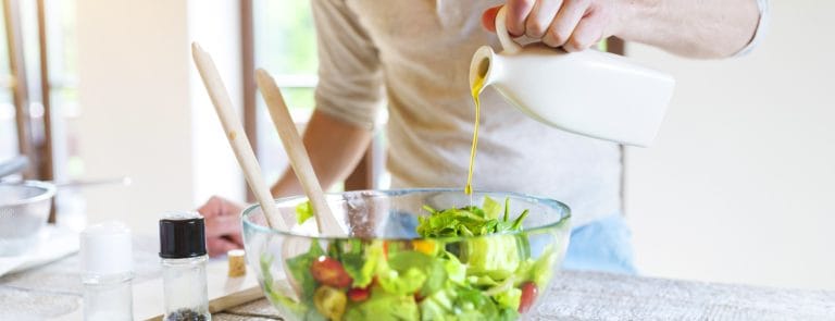 Man drizzling olive oil over a bowl of salad