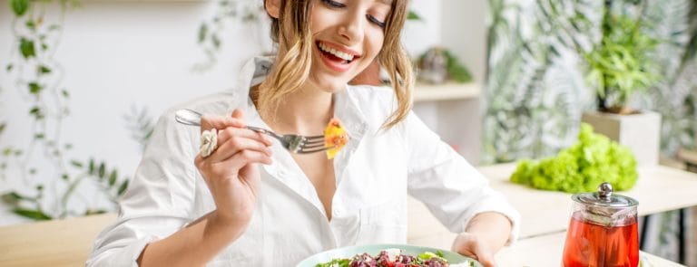 oung woman eating healthy food sitting in the beautiful interior with green flowers on the background