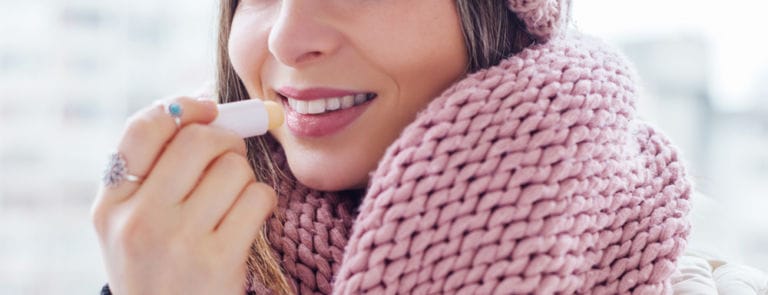 Woman wrapped in large pink scarf applying lip balm