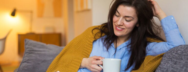 women sat on the sofa wrapped in a blanket drinking a cup of tea