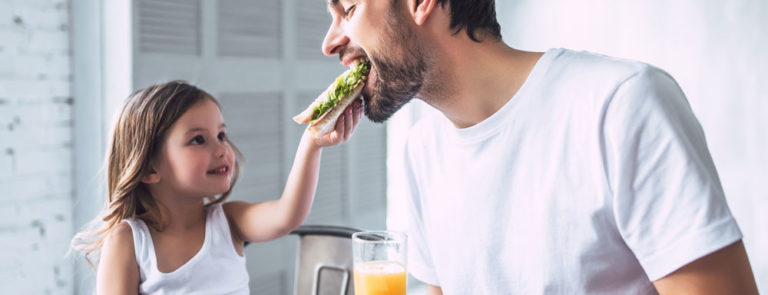 daughter feeding her father a sandwich