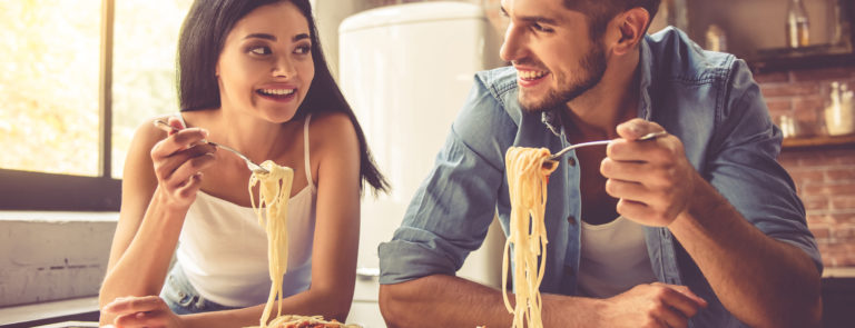 Man and woman sitting at a table eating spaghetti pasta, a carbohydrate