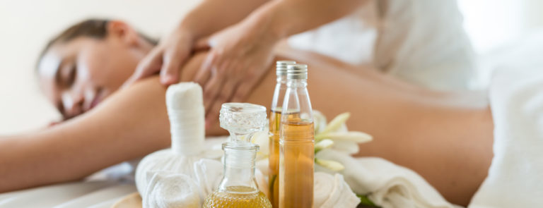 A tray with massage oils and a lady behind getting a back massage.