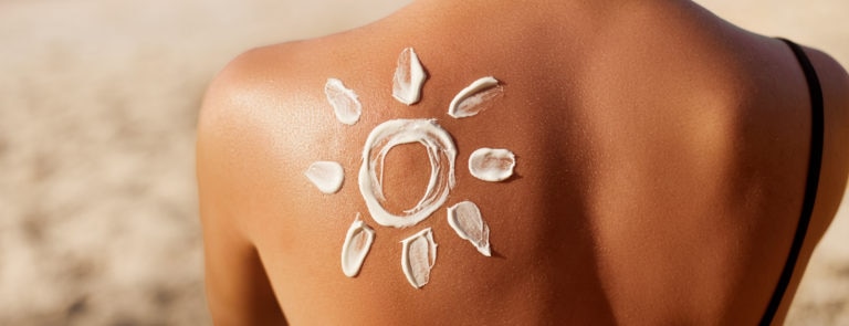 A woman on a beach, with a pattern of the sun put on with sunscreen, on her back.