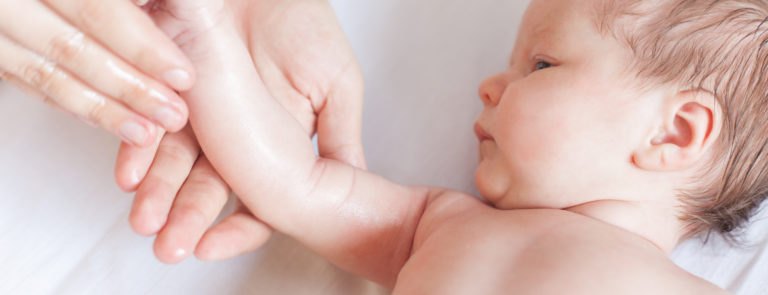 A baby laying down and having their arm massaged with oil by an adult.