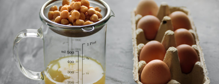 A sieve with chickpeas, draining into a jar and a carton of eggs next to it.