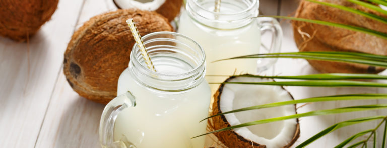 A variety of coconuts on a table with two mason jars filled with coconut water, with paper straws inside.