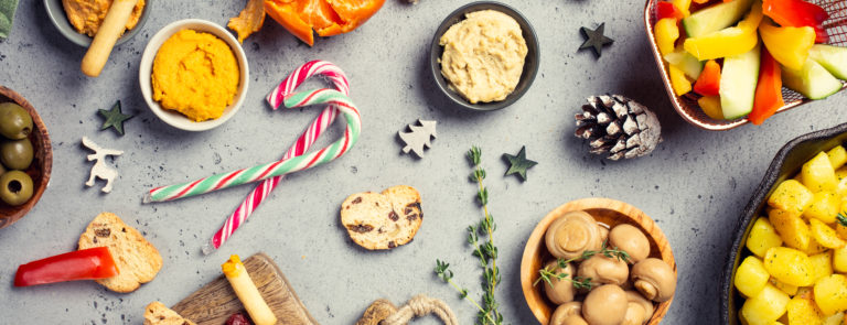 An array of vegetarian snacks such as hummus, garlic mushrooms, rye bread, oranges and candy canes on a table.