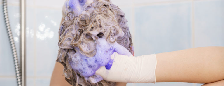 A lady wearing gloves and massaging purple shampoo into her hair.