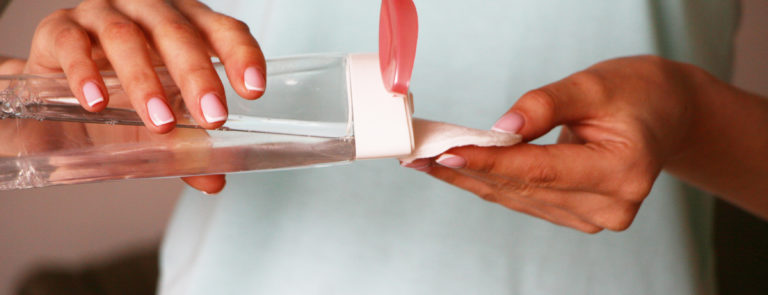 A lady pouring micellar water onto a cotton pad.
