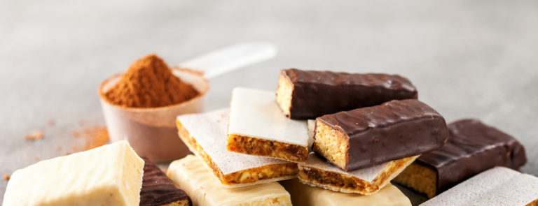 A variety of protein bars with a scoop of protein powder behind them.