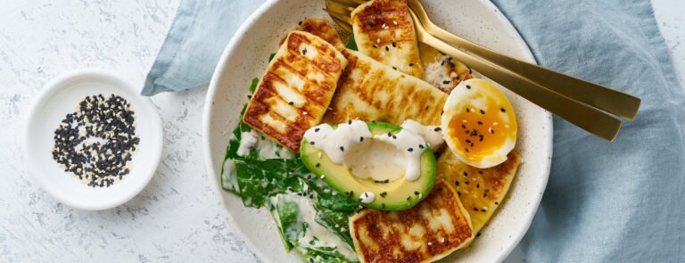 A bowl with half an avocado, brocolli, half a boiled egg and tofu.