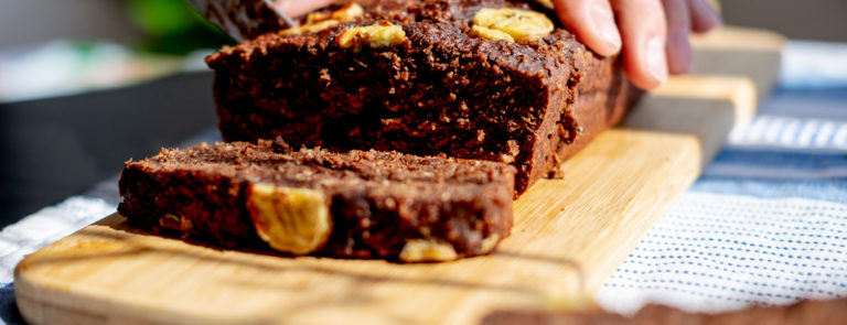 A banana bread brownie, being cut into slices on a chopping board and topped with banana slices.