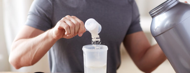 A man pouring a scoop of protein powder into a shaker filled with water.