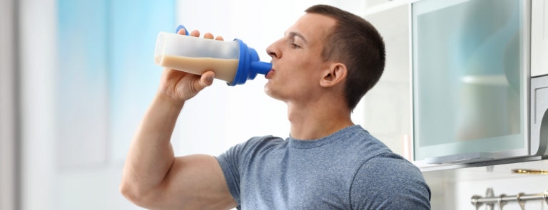 An athletic young man drinking a protein shake in the kitchen.