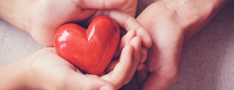 adult and child's hands holding a red heart